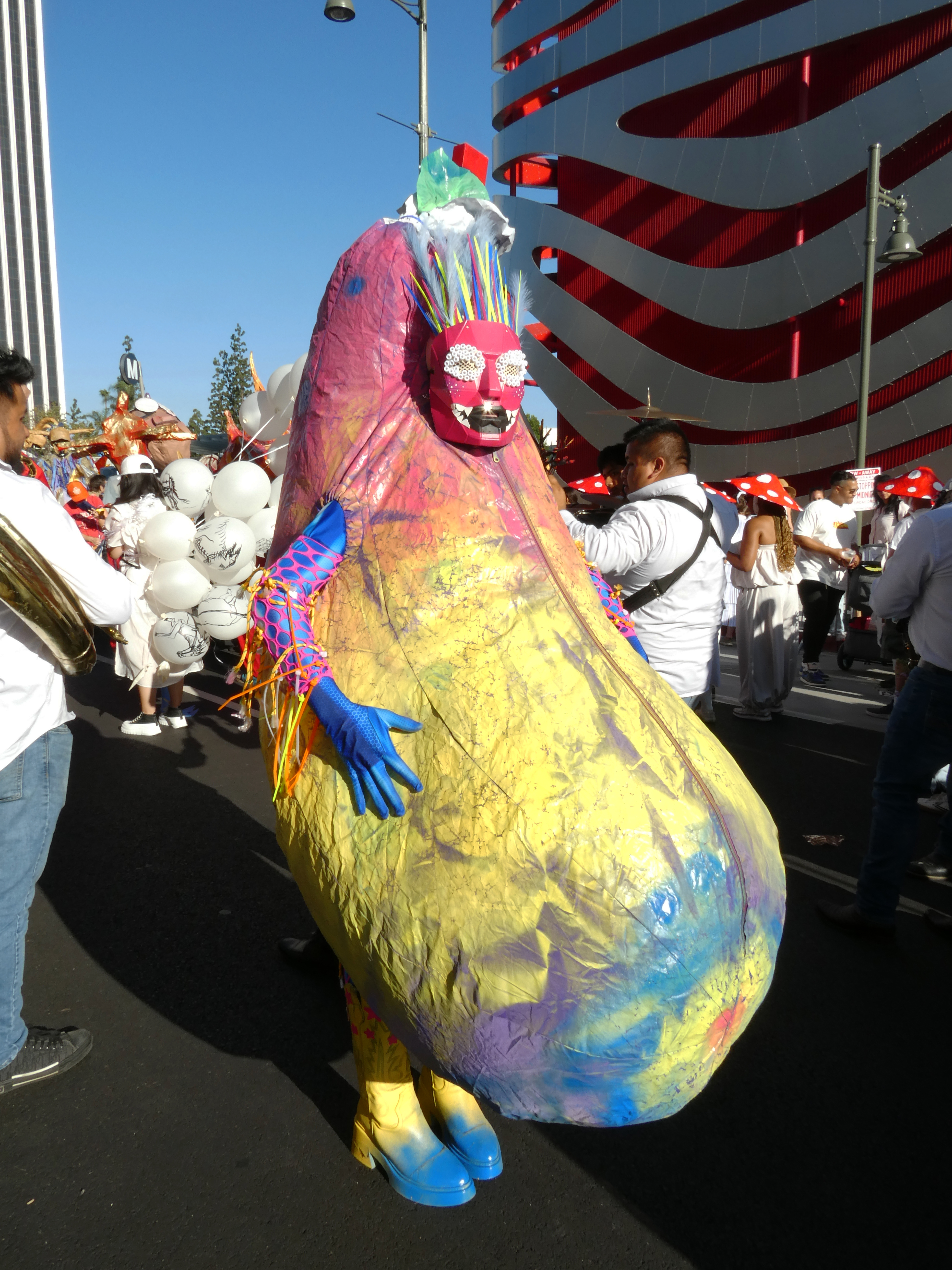 Jesse posing in a Colorful eggplant shaped inflatbale outfit in a crowded parade setting.